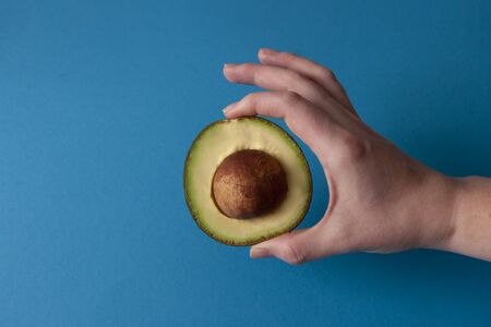 Half of avocado holding hand on blue background. Vegetable photoの写真素材