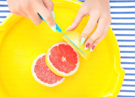 Hands close up of young woman with watermelon manicure cutting grapefruit, summer manicure nail art...