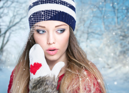 Beautiful surprised young woman wearing winter gloves and hat covered with snow flakes. Christmas...