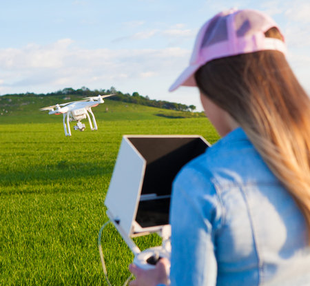 Young woman holding radio controller with tablet and sun shade flying drone uav over a field. Aerial...