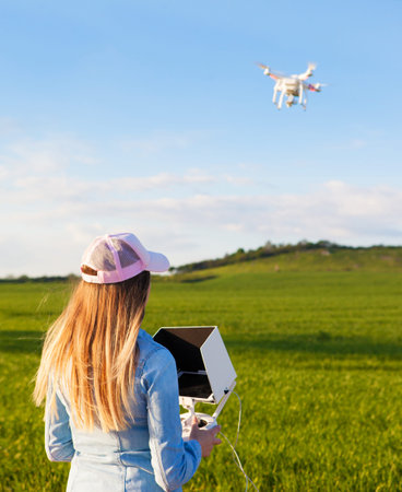 Young woman holding radio controller with tablet and sun shade flying drone uav over a field. Aerial...