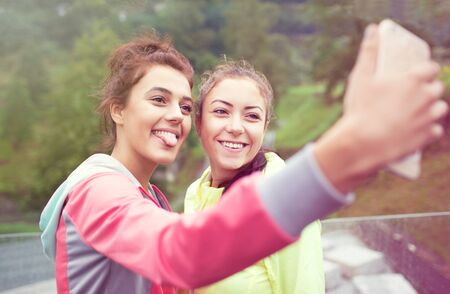 Two young women friends having fun in a park taking selfie with a smartphone. Active lifestyle and friendship conceptの写真素材