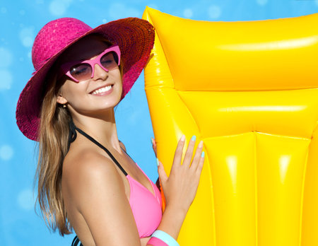 Summer beach style portrait a beautiful smiling happy young blonde woman wearing hat, bikini and sunglasses with inflatable swimming pool toysの写真素材