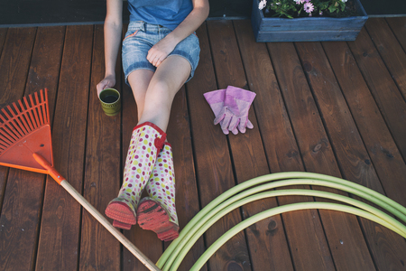 Woman with cup of coffee sitting on a wooden patio deck resting after working in the gardenの写真素材