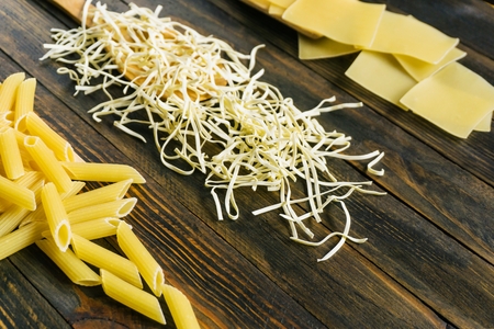 different types of pasta on a dark rustic wooden tableの写真素材