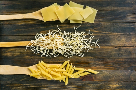 different types of pasta on a dark rustic wooden tableの写真素材