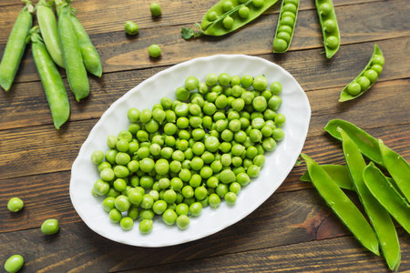 Fresh green peas in a white plate on a brown wooden background.の写真素材