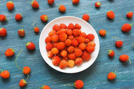 Plate with tasty ripe wild strawberries on wooden table, top view