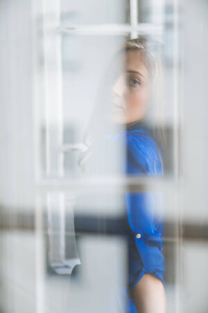 Portrait of young beautiful woman, taken through the window glass with reflectionsの写真素材