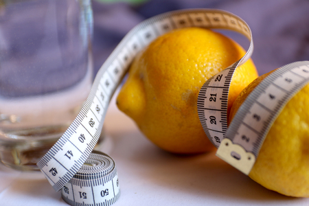 Healthy eating, drinks, diet, detox concept - close up of two lemons and water in glass with meter. Lemon water, losing weight. Loss weight fruit diet isolated. Fruit with meter, diet concept..の写真素材