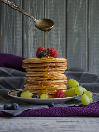 Stack of pancakes on a plate with berries and honey pouring above from a spoonの写真素材