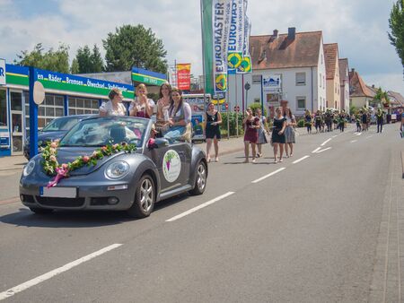 Kirchheimbolanden,Rheinland-Pfalz/Germany-06 23 2019: Small decorated cabriolet carrying four smiling girls in dirndles sitting on top, with glasses of wine in hands, followed by parade processionのeditorial素材