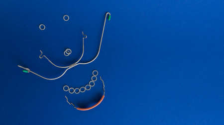 Orthodontic devices,removable metal braces and rubberized flesh-colored plastic cap for upper and lower teeth,dental rubber bands laid out in shape of smiling face on dark blue backdrop.Copy space.の写真素材