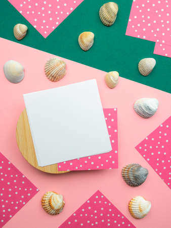Flatlay, close up top view square note sheets on round wooden base, dark green diagonal paper, ivory seashells scattered, corners of pink paper white polka dots on perimeter. Design pattern copy spaceの写真素材