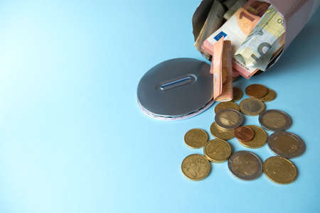 Close-up open,cut tin piggy bank from which money,cash,euro banknotes,coins spilled out,light blue background.Concept of financial crisis,waste of stocks,spending savings, selective focus, copy spaceの写真素材