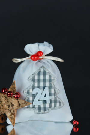 Forth Advent card.Fabric gray gift bag number 24,tree bark star,shiny red balls of decoration like berries on dark background,homemade recycable organic concept,copy space. Vertical Christmas decorの写真素材