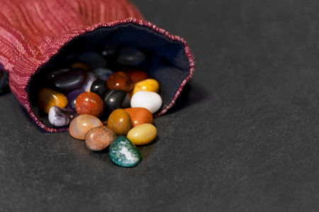 Handful of small semi-precious stones spilling out of homemade red striped cloth bag sewn with white...