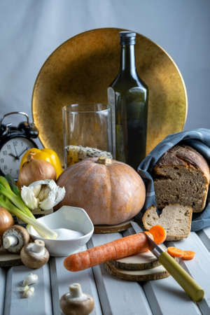 Close-up food still life,ingredients for home recipe self cooking in limited time.Sliced carrots,freshly baked hot rye bread wrapped in textile,alarm clock in background,olive oil,pumpkin,golden dishの写真素材