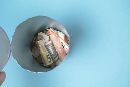 Close-up opened tin, piggy bank of euro small change banknotes, coins. Concept of spending savings, poverty and inflation, collapse of ruble exchange rate. Blue background.Selective focus,copy space.の写真素材