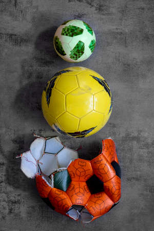 Pyramid of three soccer balls, torn orange big old ball, used yellow, new green small one for mini football. Vertical close up abstract sports pattern, gray background, copy space. Evolution concept.の写真素材