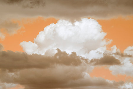 Wild stormy beautiful orange sky with light dark brown contrasts. Fluffy cumulus clouds in different layers. Surreal abstract colorful sandy background, wind change in cyclone on sundown. Copy space.の写真素材