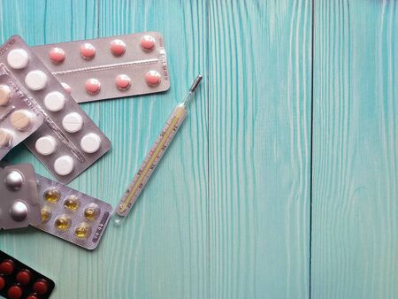 Tablets and a mercury thermometer. Pharmaceutical tablets and medical thermometer isolated on a turquoise wooden background, top view with plenty of space to copy your text.の写真素材