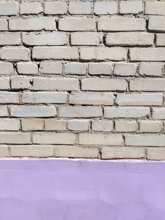 Texture of a city brick wall with lilac stucco painted lower part. Gray brick background, grungy gray texture with bright bottom. Place for text.の写真素材