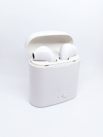 White wireless headphones and a charging case on a white background. A pair of modern wireless headphones inside the charging case. Space for textの写真素材
