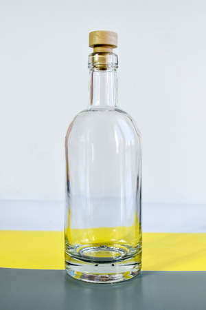Empty transparent glass bottle. Bottle with cork, lit by the sun, stands on a gray-yellow backgroundの写真素材