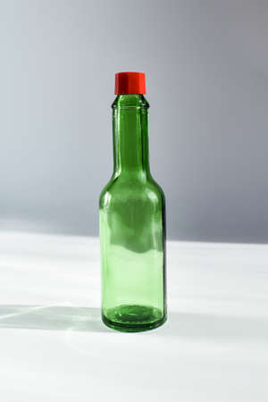 dark green decorative bottle with a red cap on a gray background, lit by the sun. Small green bottle for sauceの写真素材