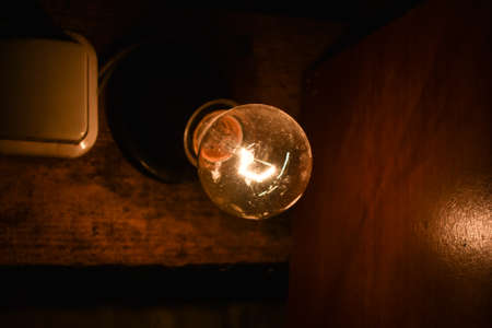 Light bulb next to the switch on the wall in a dark room. Close up vintage glowing light bulbs, Edison's lamp on the dark background with copy space. Bright idea concept.の写真素材
