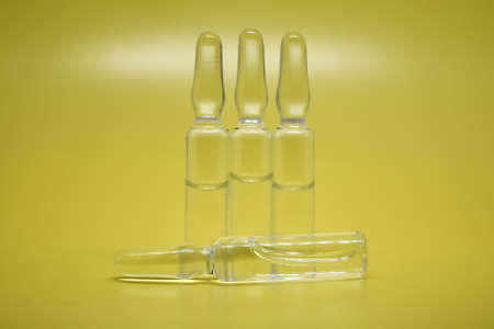 Transparent medical ampoules close-up, selective focus. A lot of glass ampoules on a yellow background. Medical concept.の写真素材