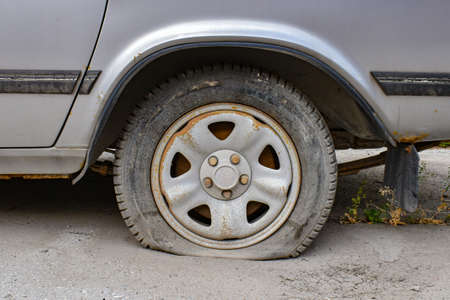 Old gray car with a punctured wheel outdoors. Damaged flat tire of a car. Abandoned car with a flat tire.の写真素材