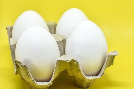 Fresh white eggs in a cardboard box on a yellow background. Chicken eggs in sustainable packaging...