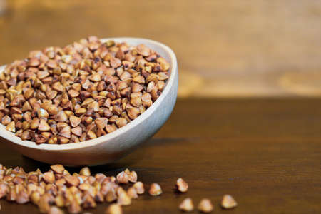 Buckwheat in a wooden spoon on a brown wooden background. Healthy food concept, vegetarian food. Diet foods. Copy space. Wooden spoon with buckwheat on a wooden table. Selective focus ofの写真素材
