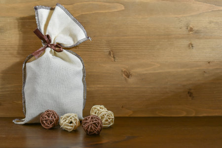 A canvas bag with gifts next to small wicker decorative balls, on a brown wooden background. Copy...