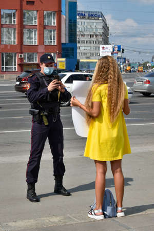 Novosibirsk, Russia - 08.08.2020: A girl went to a solo picket near the Opera House in support of protesters in Khabarovsk with a poster. The policeman takes pictures of her with a cell phone.のeditorial素材