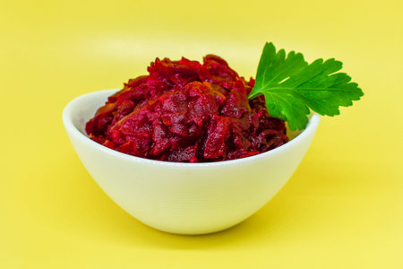 Grated beets. Fresh beet salad in white bowl isolated on yellow background. Healthy food concept,...