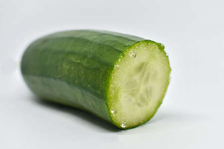Green cucumber. Sliced ââpiece of fresh cucumber on a white background. Cucumber juice is released when cut. Single cucumber or zucchini. Vegetarian, healthy diet food. Ingredient for salad.の写真素材