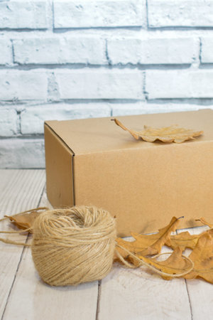 Cardboard box, autumn oak leaves and a ball of rope on the background of a wooden table top and a...