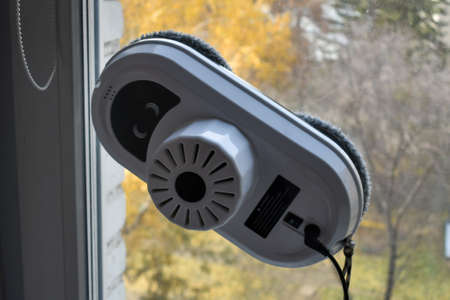 Robot for cleaning windows and ceramic tiles against a background of a window and an autumn landscape. Intelligent home appliances, washing robot for outdoor and indoor cleaning of windows.の写真素材