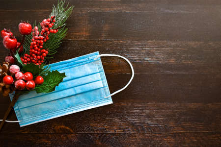 Medical mask and Christmas decor on a brown wooden background. New Year / Christmas layout, top view, place for text. The concept of protection against viruses, seasonal incidence, pandemic.の写真素材