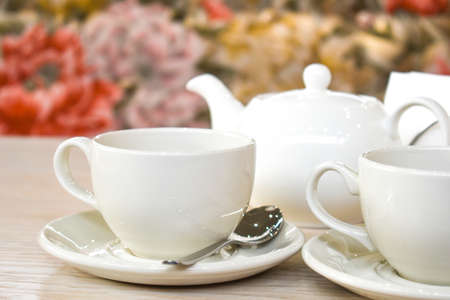 White cup and teapot on the background of a cozy interior in the restaurant. A couple of tea on the table. Space for textの写真素材