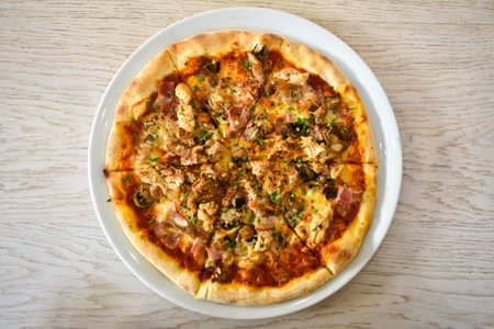 Baked pizza with mushrooms, bacon and cheese in a white dish on a light wooden table. Top view....