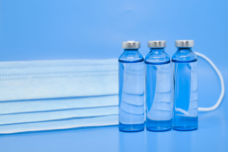 Transparent medical ampoules and a protective medical mask on a light blue background. Concept:...
