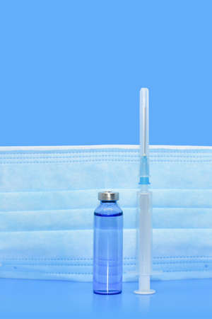 Transparent medical ampoules, syringe and protective mask on a light blue background. Concept: medicine, injections, vaccination against covid-19, seasonal diseases. Protection during a pandemic.の写真素材