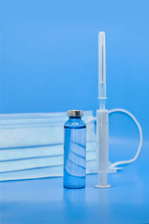 Transparent medical ampoules, syringe and protective mask on a light blue background. Concept: medicine, injections, vaccination against covid-19, seasonal diseases. Protection during a pandemic.の写真素材