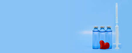 Glass medical ampoules, syringe and red heart on a light blue background. Healthcare concept: saving lives, COVID-19 vaccination, heart treatment. Large format banner with space for text.の写真素材