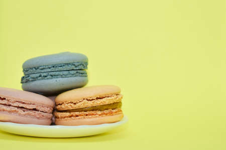 Multicolored macaroons in the form of a tower on a yellow background. Colorful greeting card with delicious almond cookies. Sponge cakes on top of each other. Spaces for text, copy space.の写真素材