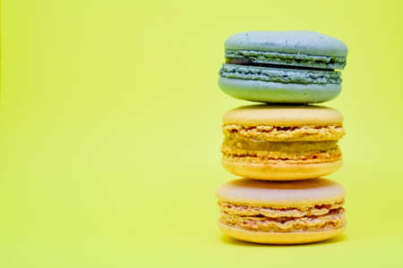 Multicolored macaroons in the form of a tower on a yellow background. Colorful greeting card with delicious almond cookies. Sponge cakes on top of each other. Spaces for text, copy space.の写真素材